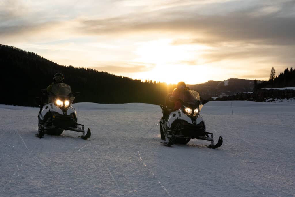 Snowmobiles ride across a snowy expanse in the sunset