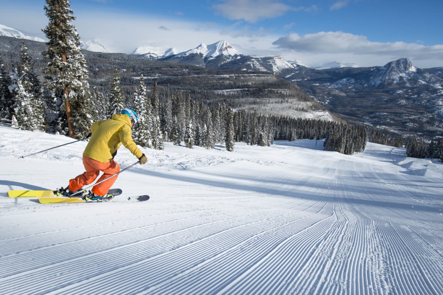 Skier in yellow and orange skiing down a groomer run