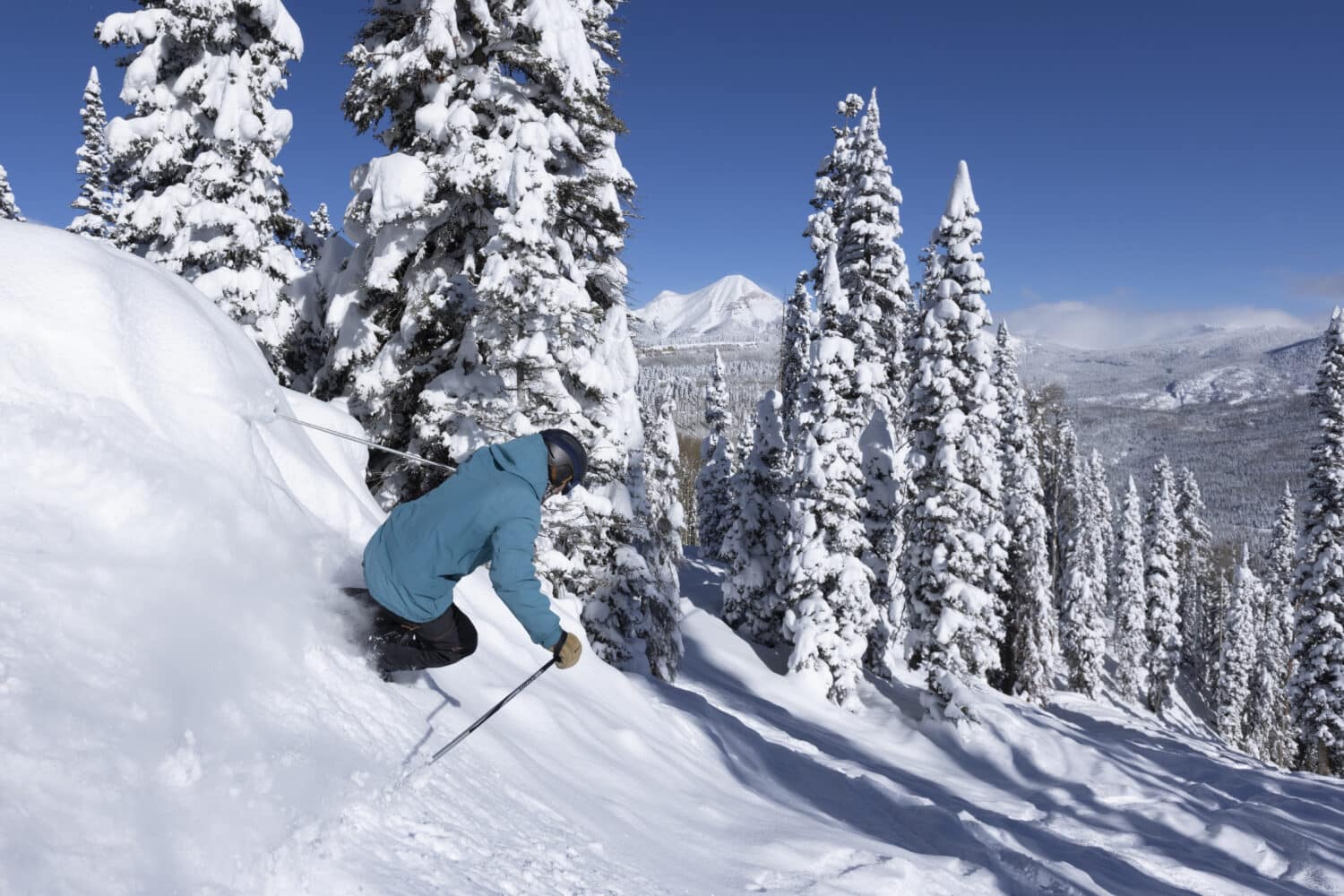 Skiers rides down a headwall of powder on a bluebird day