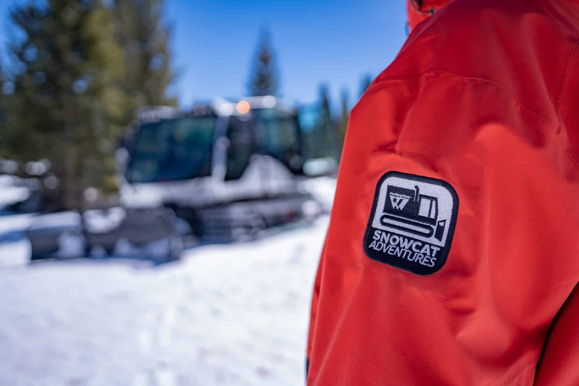 Close up of snowcat adventures jacket with scenic snowcat out of focus in the background