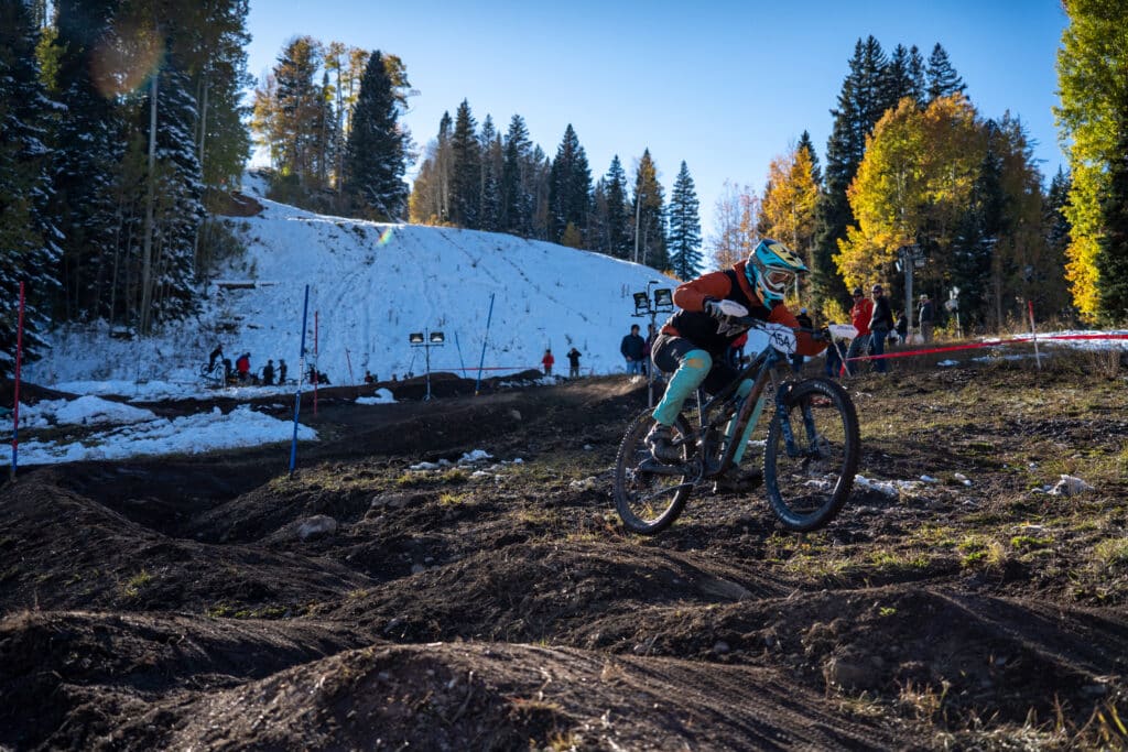 Collegiate racers flys over a double on the duel slalom course as bright orange and yellow aspens glowing the sunset light.