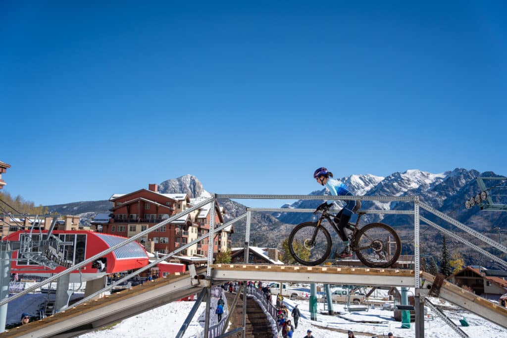 Fort Lewis Skyhawks athlete rides over the fly over with Purgatory's base area and snowy peaks in the background.