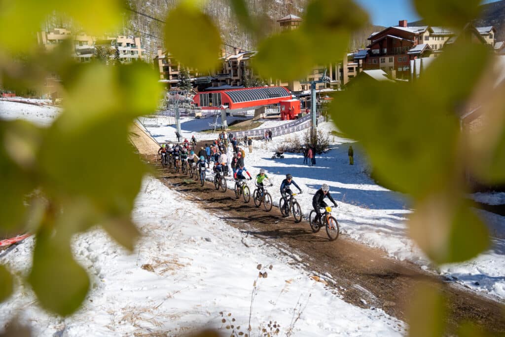 Collegiate racers race for position out of the base area of Purgatory Resort with fall colored aspen leaves in the foreground.