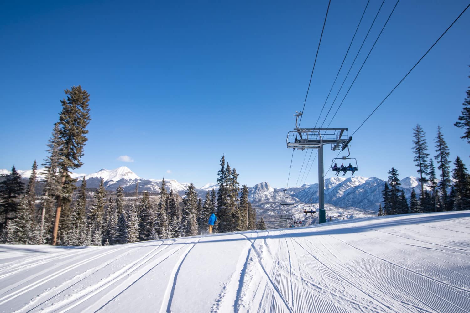 Three skiers ride the lift above a snowboarder