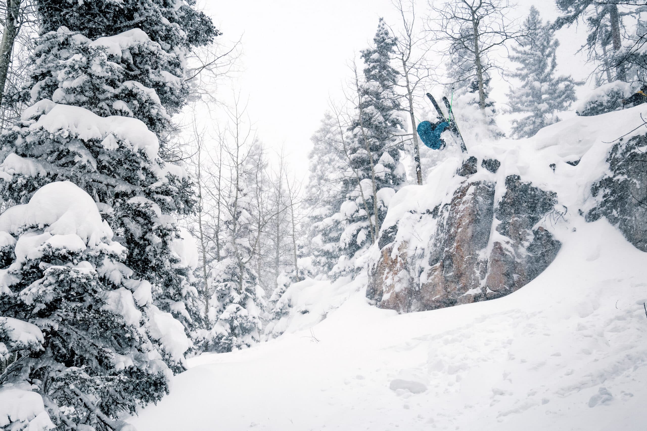 Skier front flipping off a cliff on a powder day