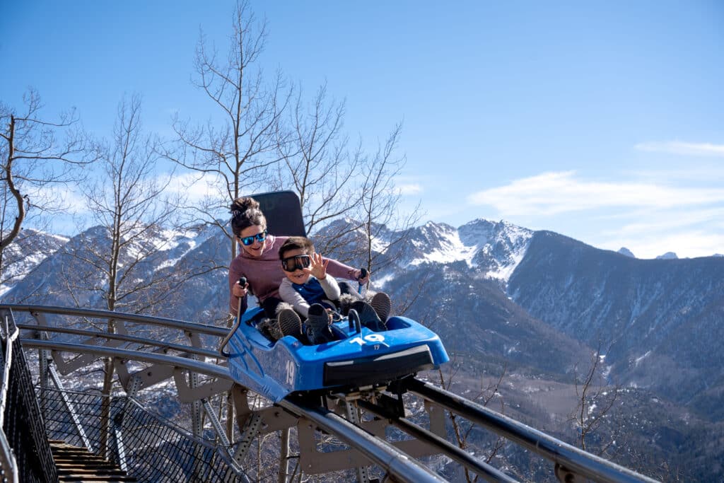 Mother and son race down the Inferno Mountain Coaster on a bluebird winter day