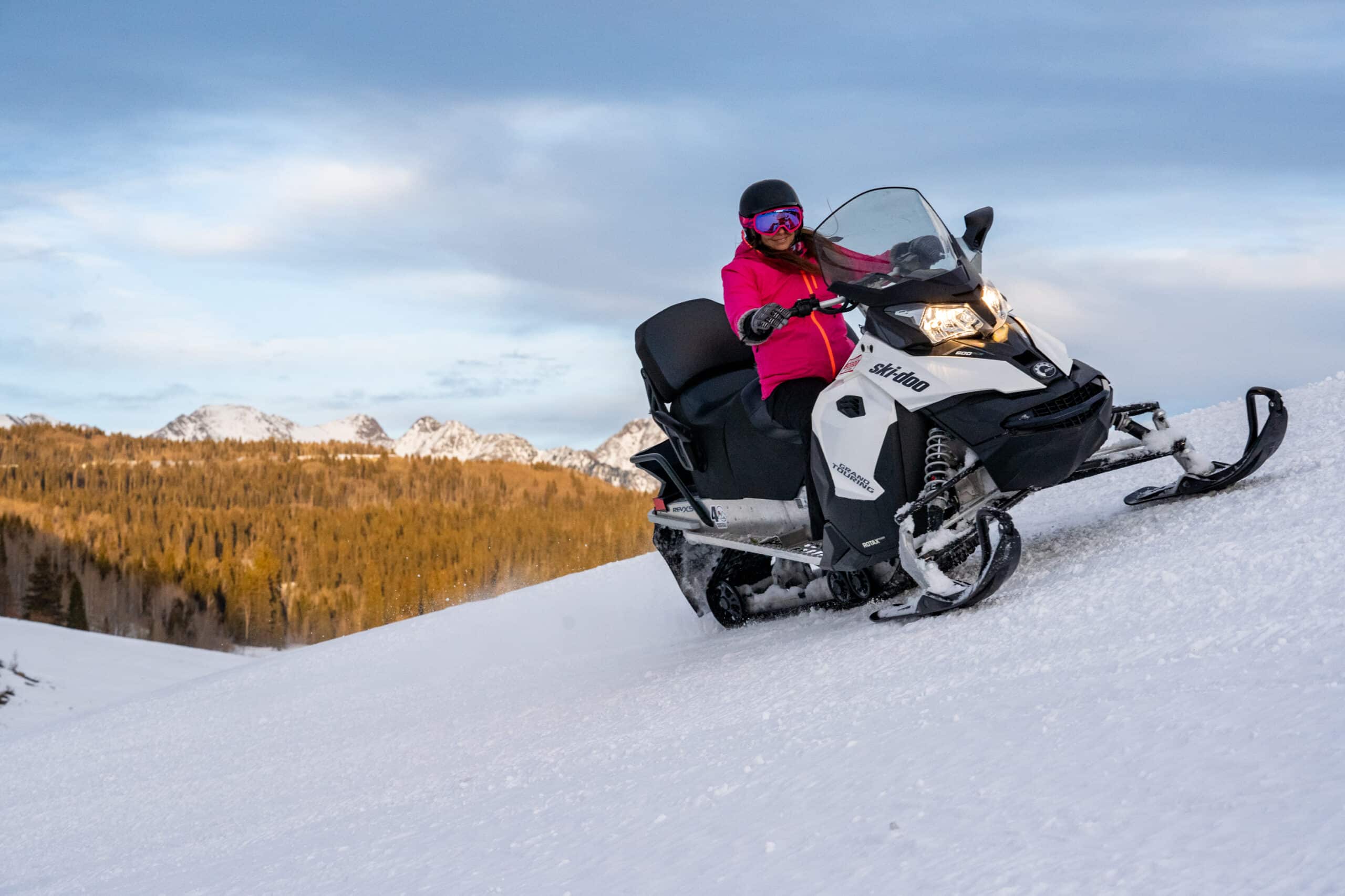Female rider smiles as she takes a huge bank turn on a guided snowmobile tour