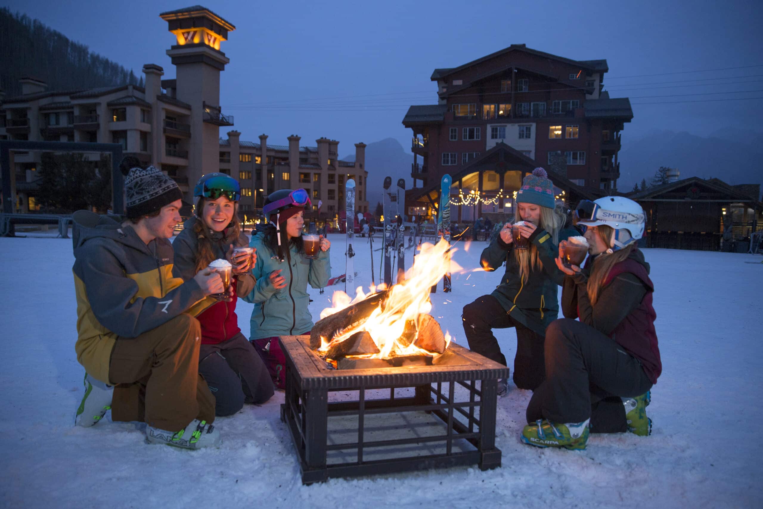 Friends enjoy hot cocoa around a fire on a snowy evening