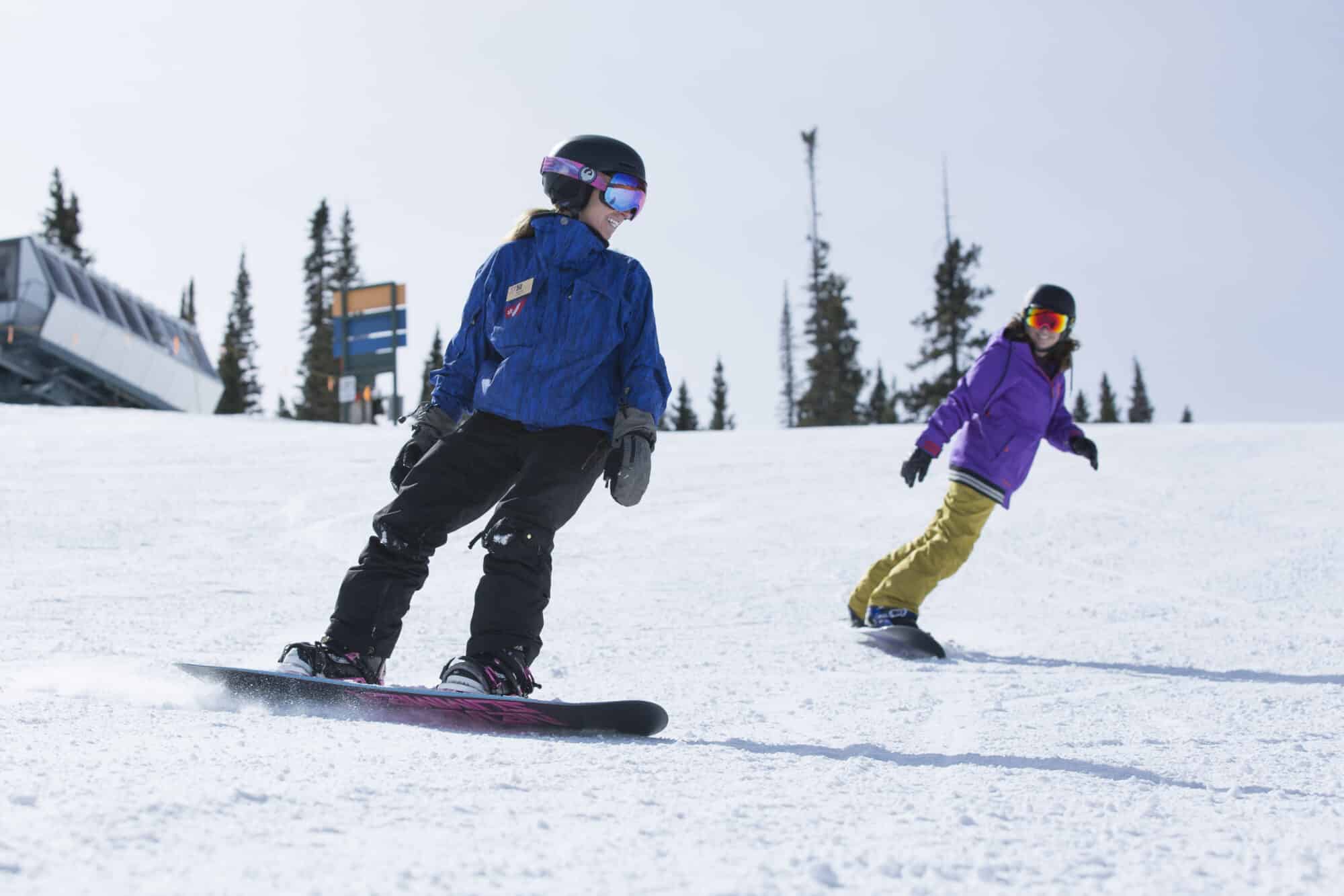 A snowboard instructor teaches a student on the slopes