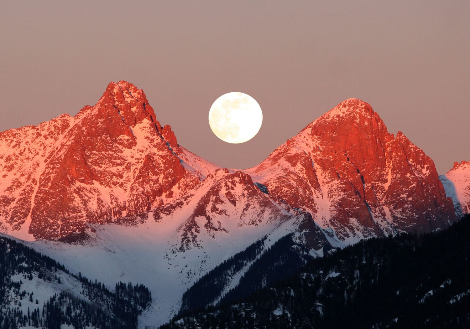 A full moon rises between two peaks