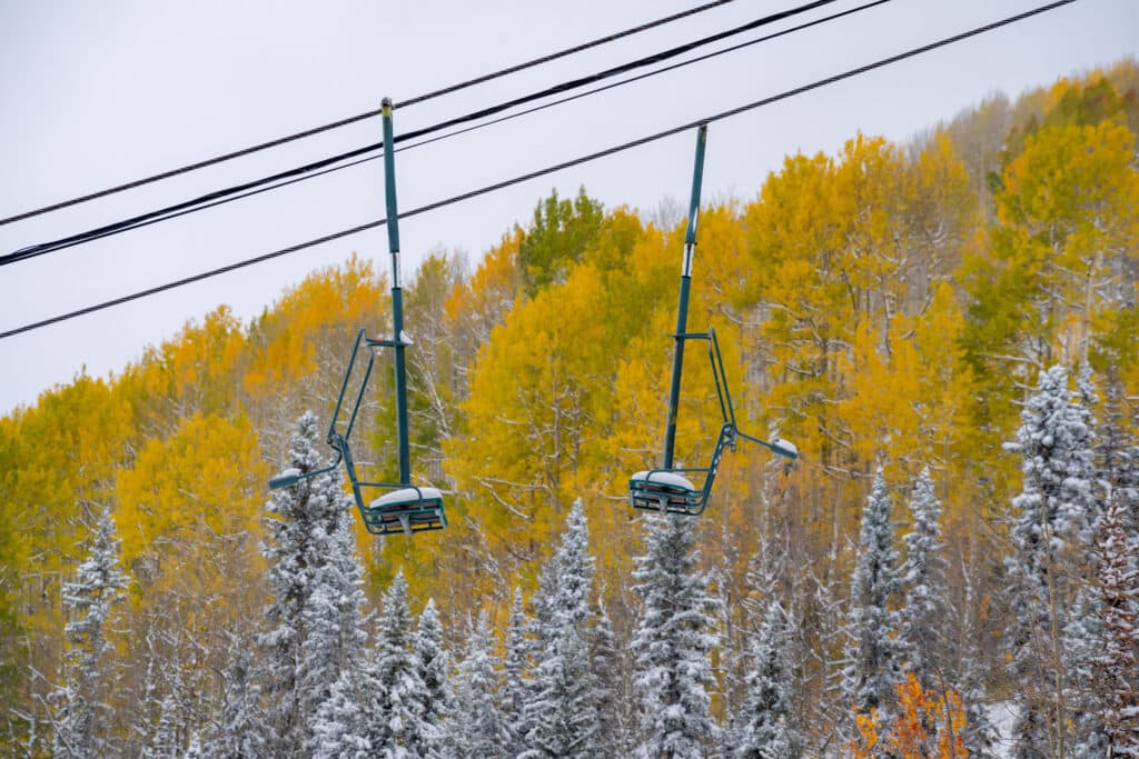 Chairlift covered with snow while beautiful fall aspens peak in color in the background.