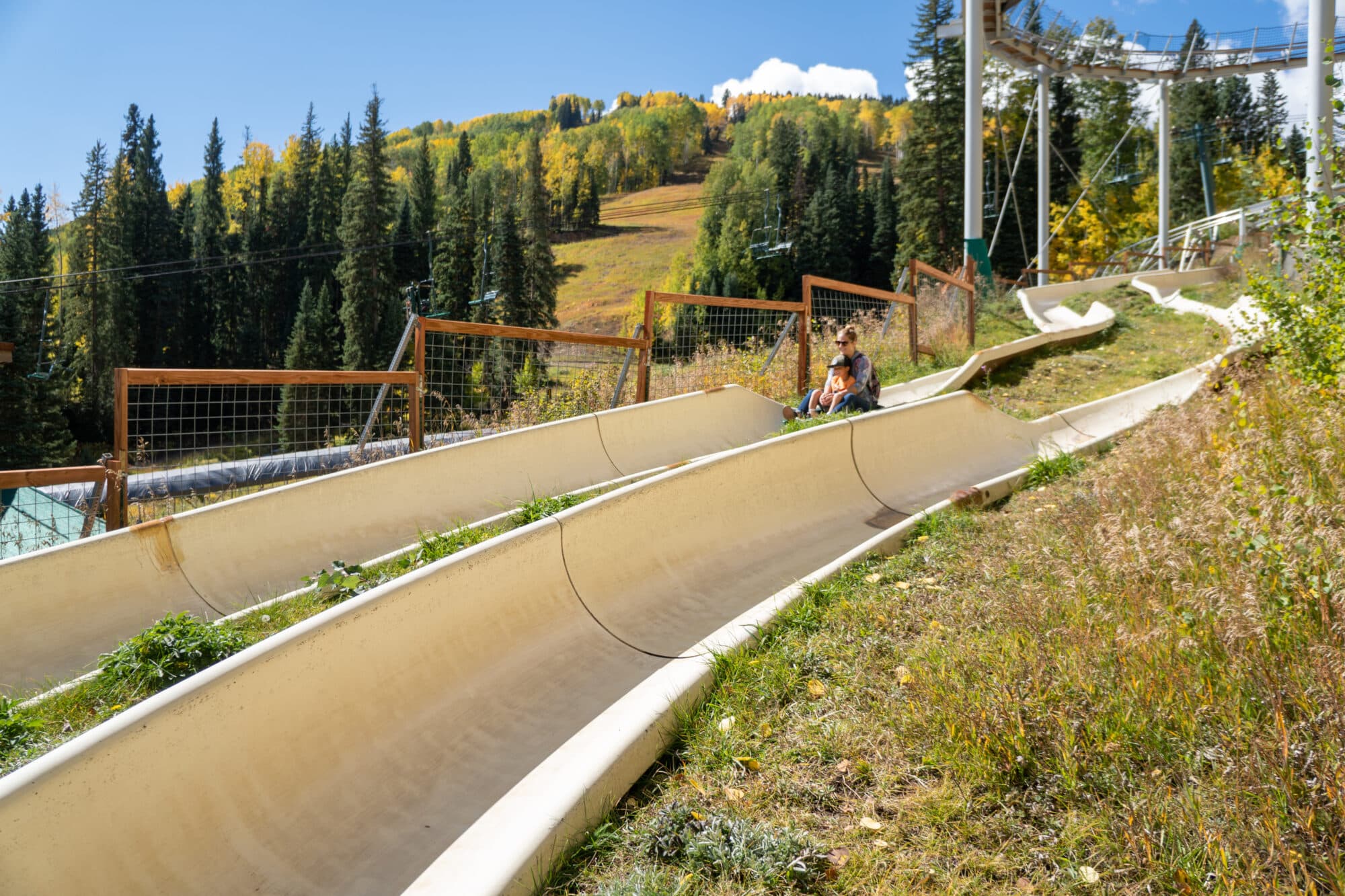 Mom and son glide down the alpine slide in autumn