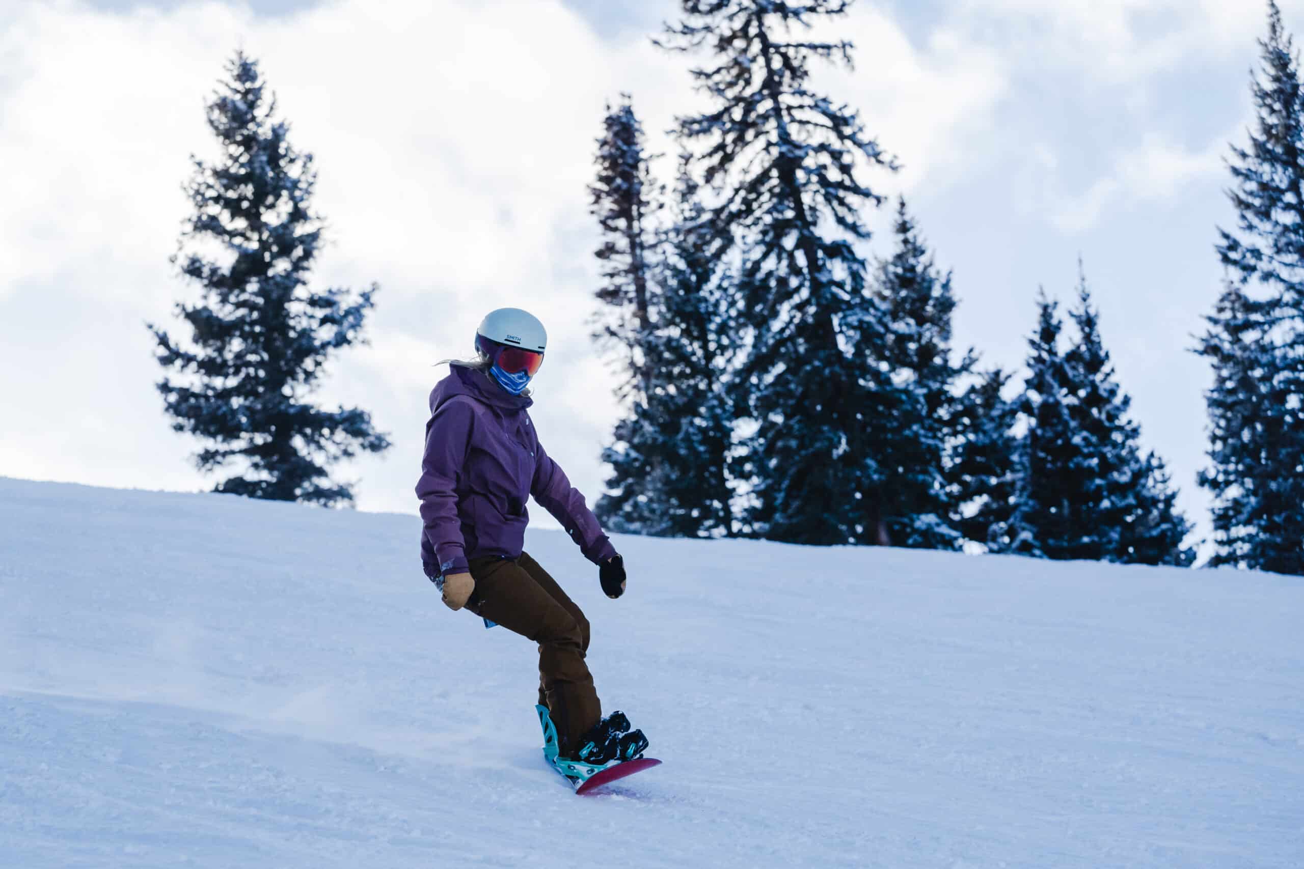 A woman snowboards down a slope with trees in the background