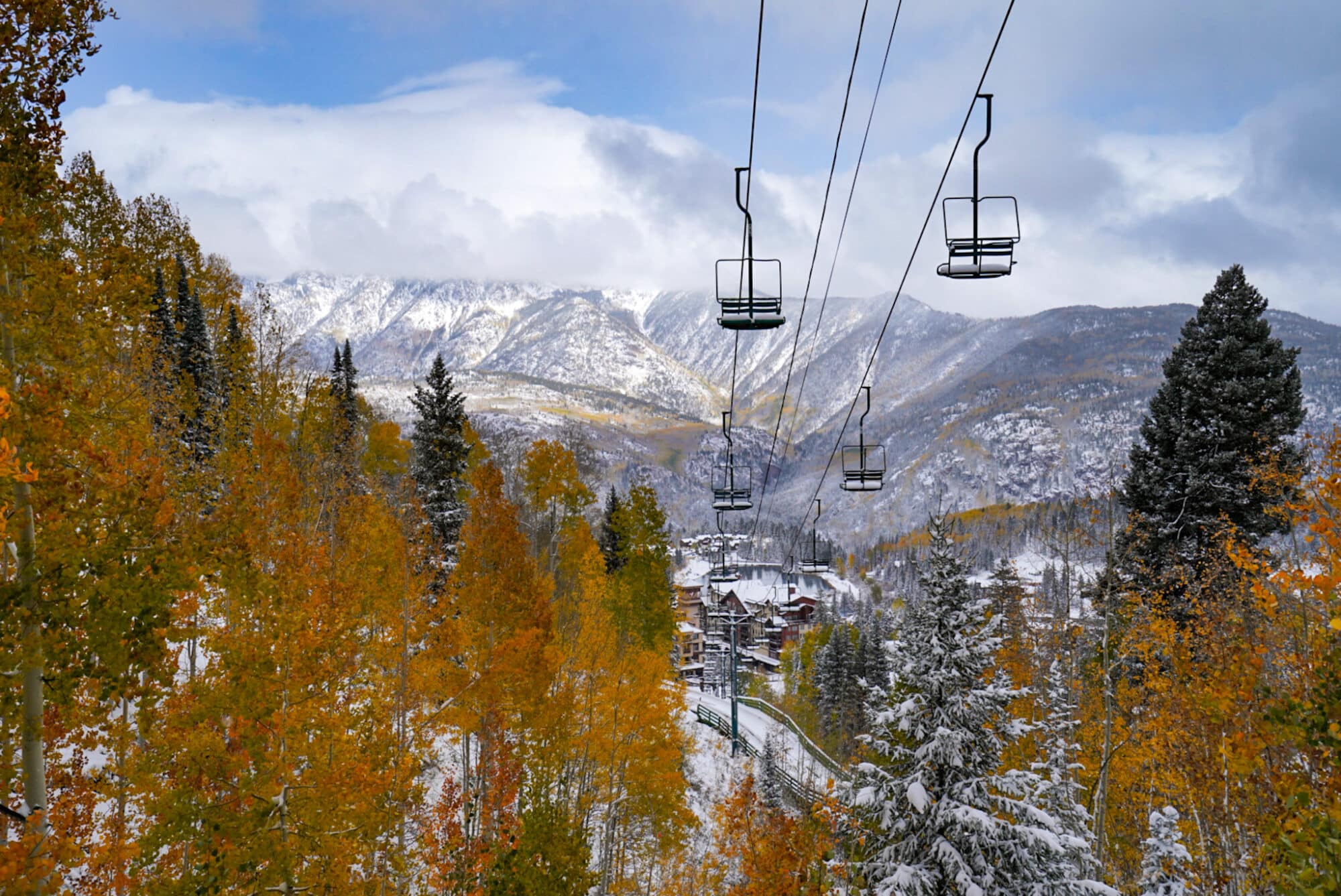 A chair lift looks out over the first snow of the season coating the San Juan mountains and autumn leaves