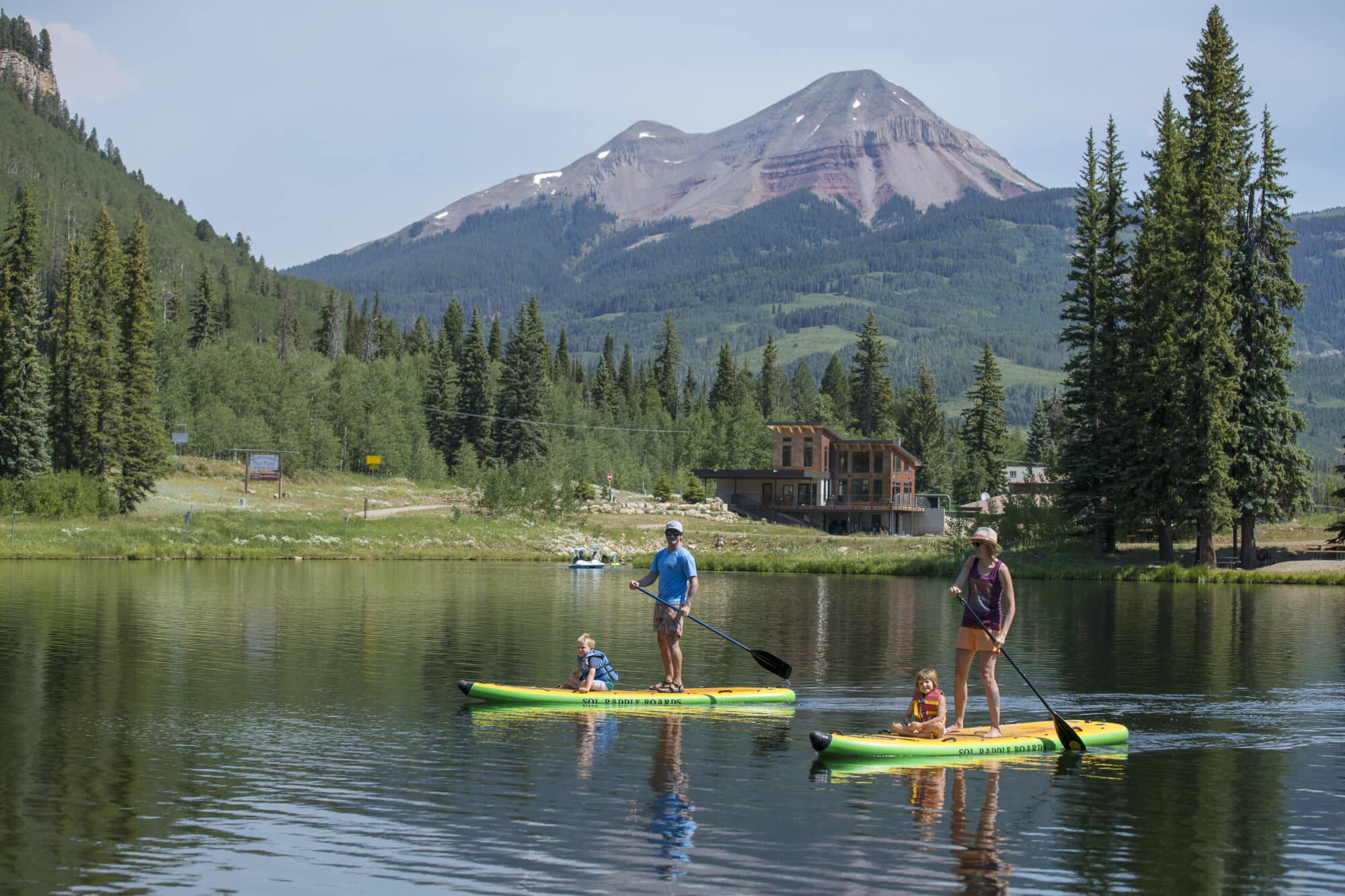 Family paddle boards around twilight lake on a summer day