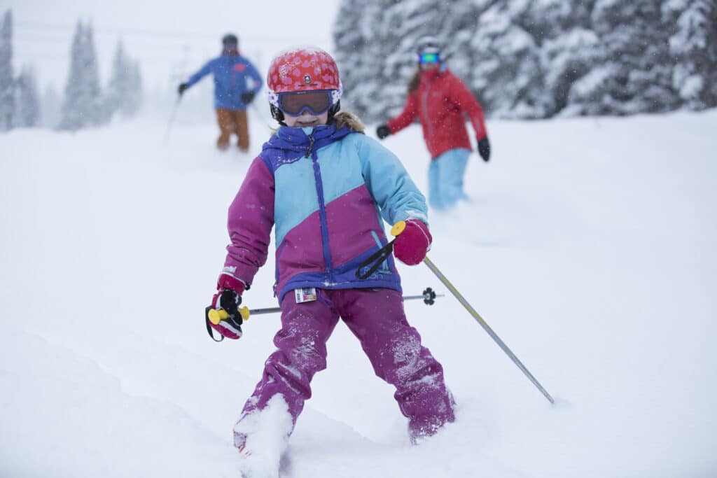 A little girl in a pink and blue ski suit pizzas down a snowy slope