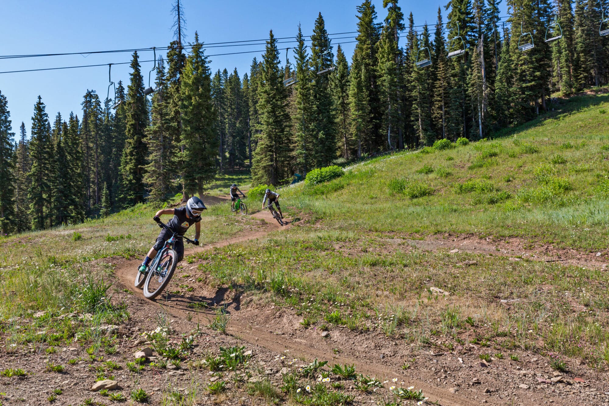 Group of advanced mountain bikers ride down the mountain in a line