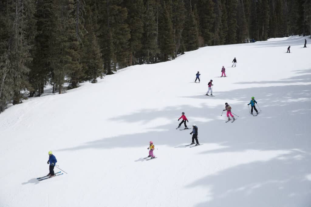 Kids group lessons follow instructor down the mountain in a single file line