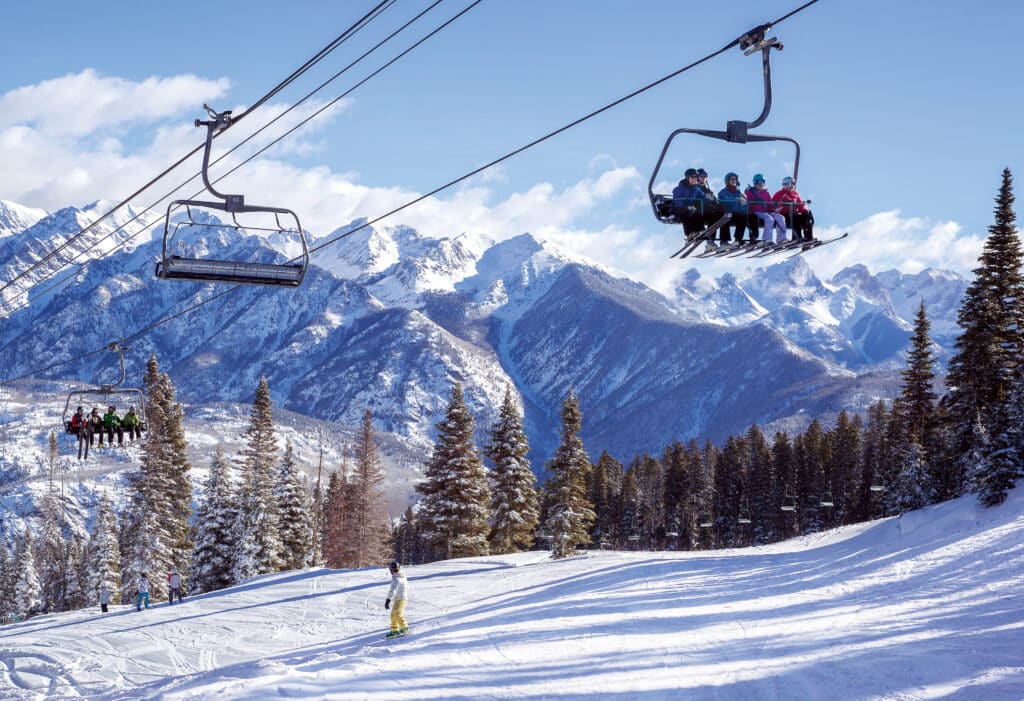 Group of skiers rides up the Purgatory Express lift with the Needles Mountain Range in the background