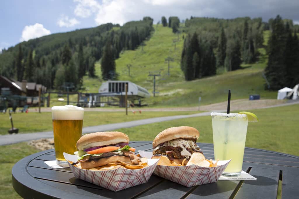 Burgers and beverages sit on a table with the Purgatory Express ski lift in the background