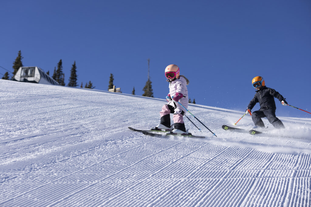 Young kids ski down fresh corduroy