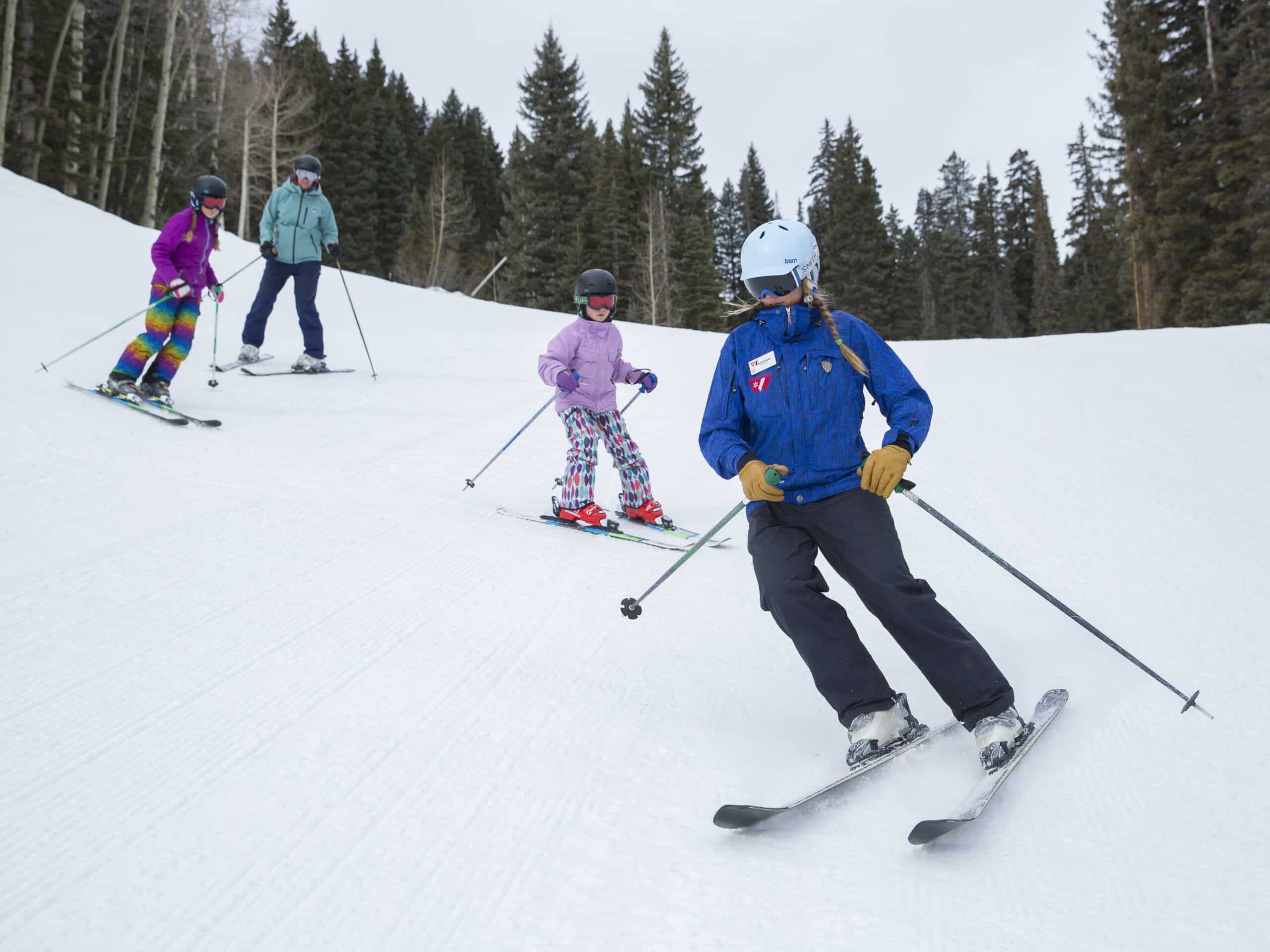 Young kids and mom follows ski instructors turns