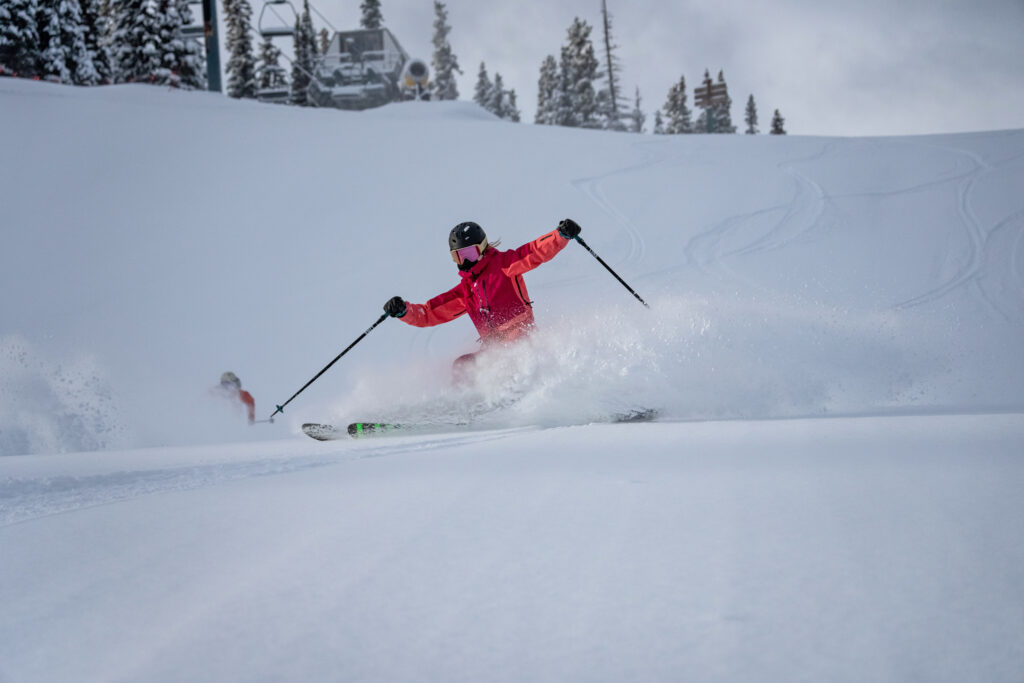 skier in pink slashes snow on a groomer