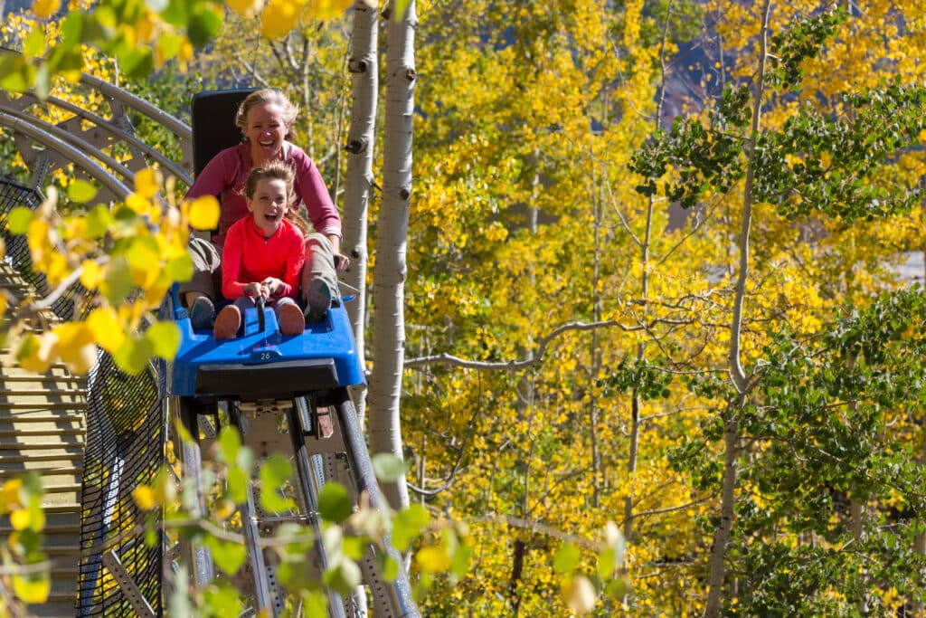 A woman and her daughter laugh as they enjoy riding the Inferno Mountain Coaster through the golden aspens