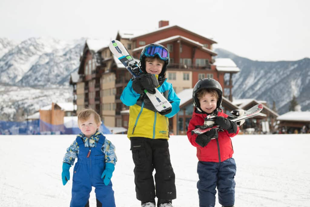 Kids walk across the base area with skis in front of Purgatory Lodge 