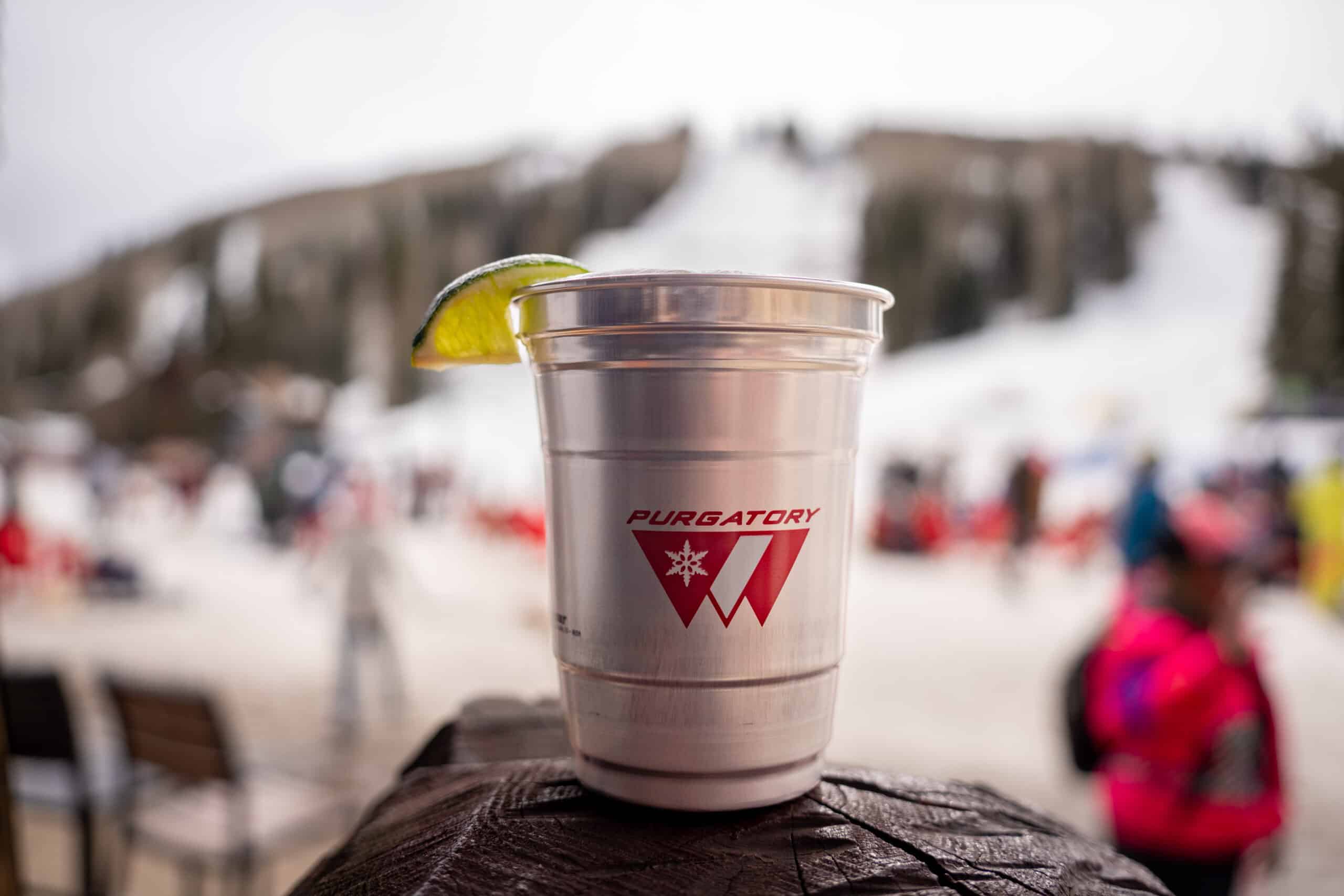 A Purgatory logo aluminum cup sits with a lime wedge in front of the snowy mountain