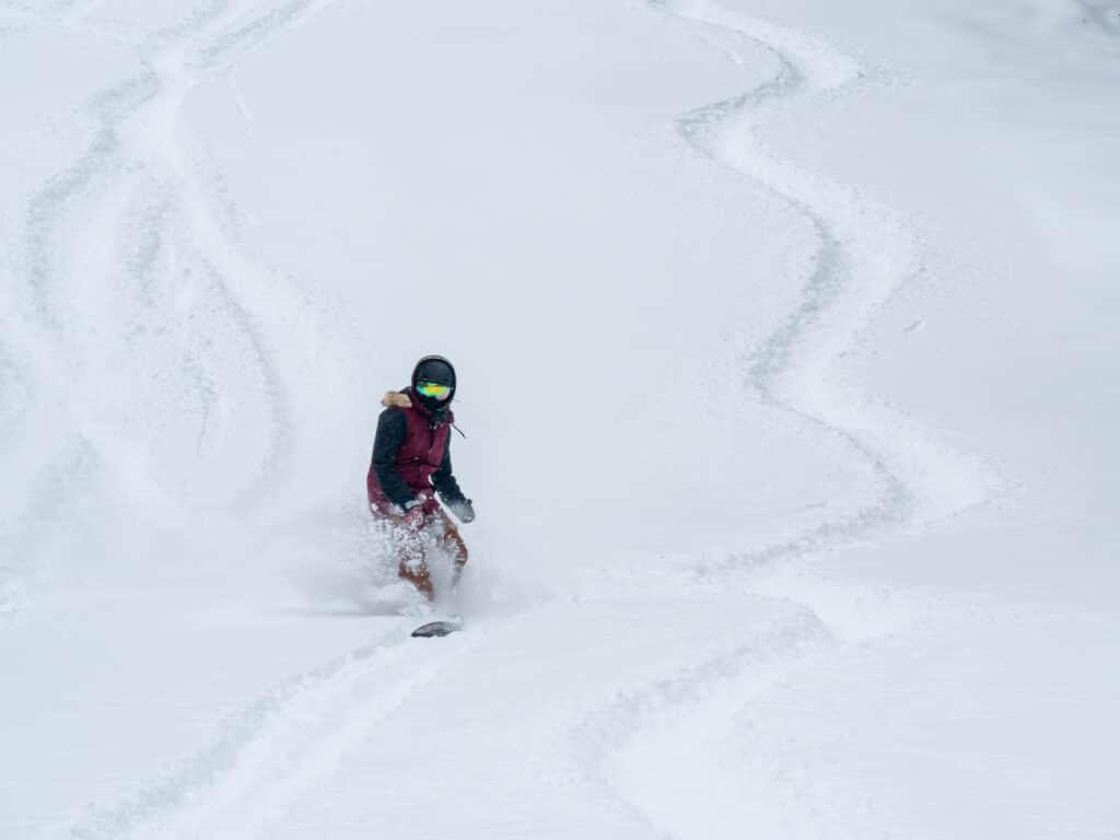A Snowboarder leaves tracks in the powder on a snowy slope
