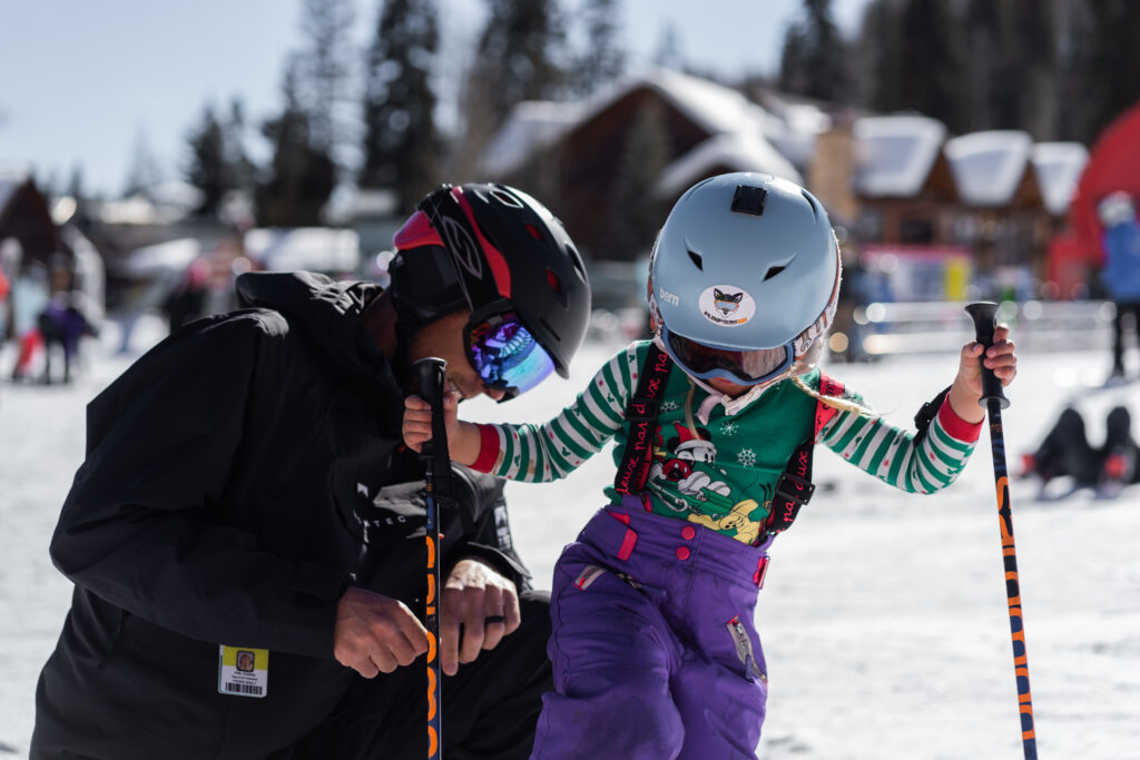 A father helps his daughter put her skis on