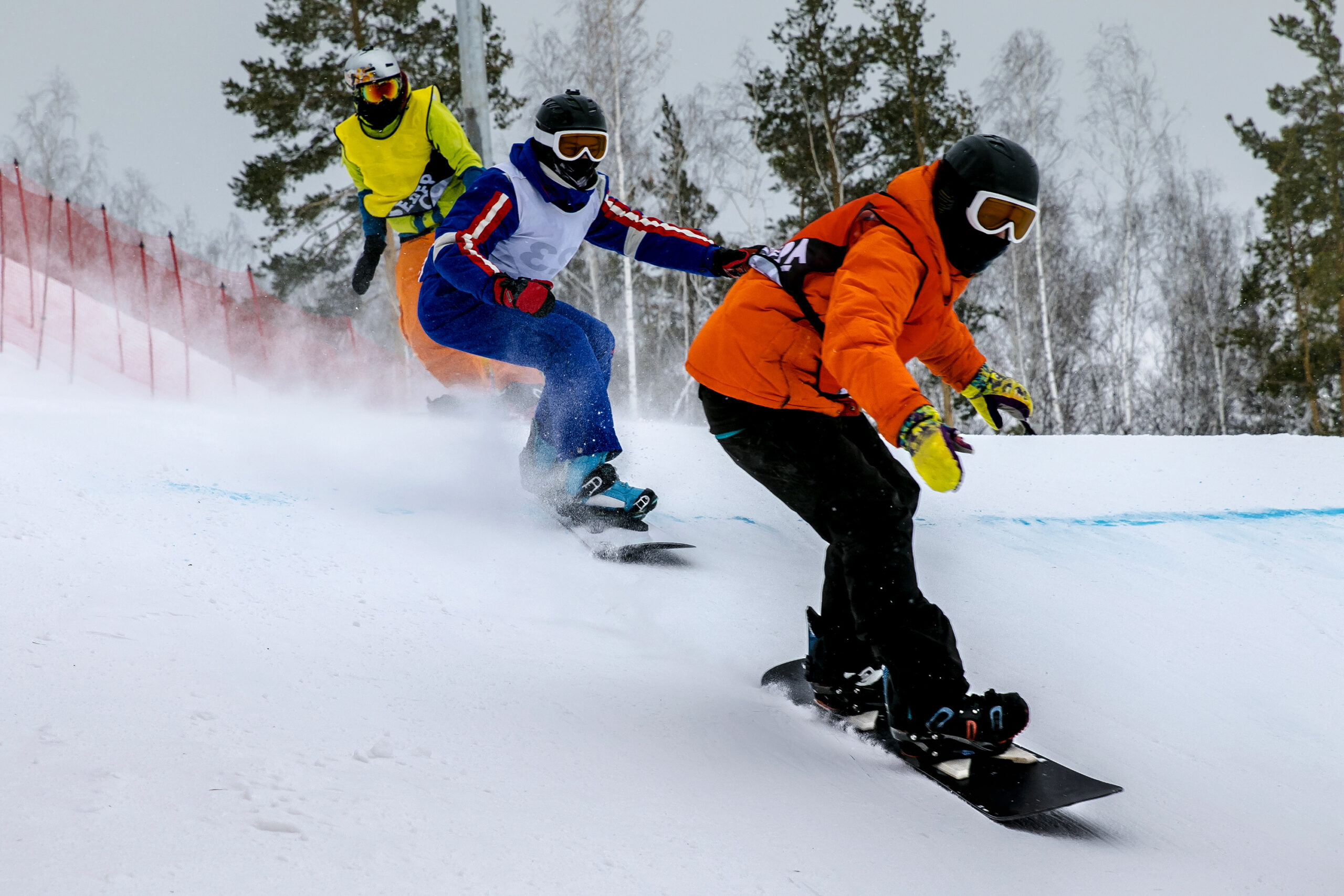 Snowboarders race one another down a snowy slope in a boardercross race