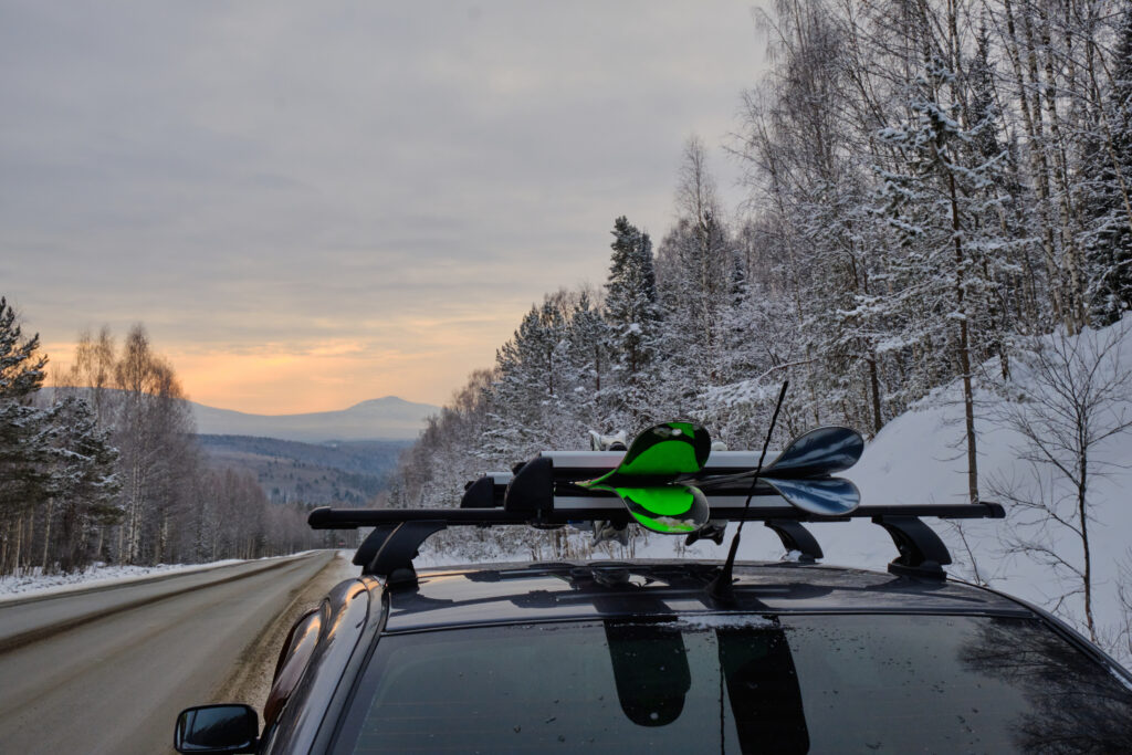 A car with skis strapped to the top drives down the road