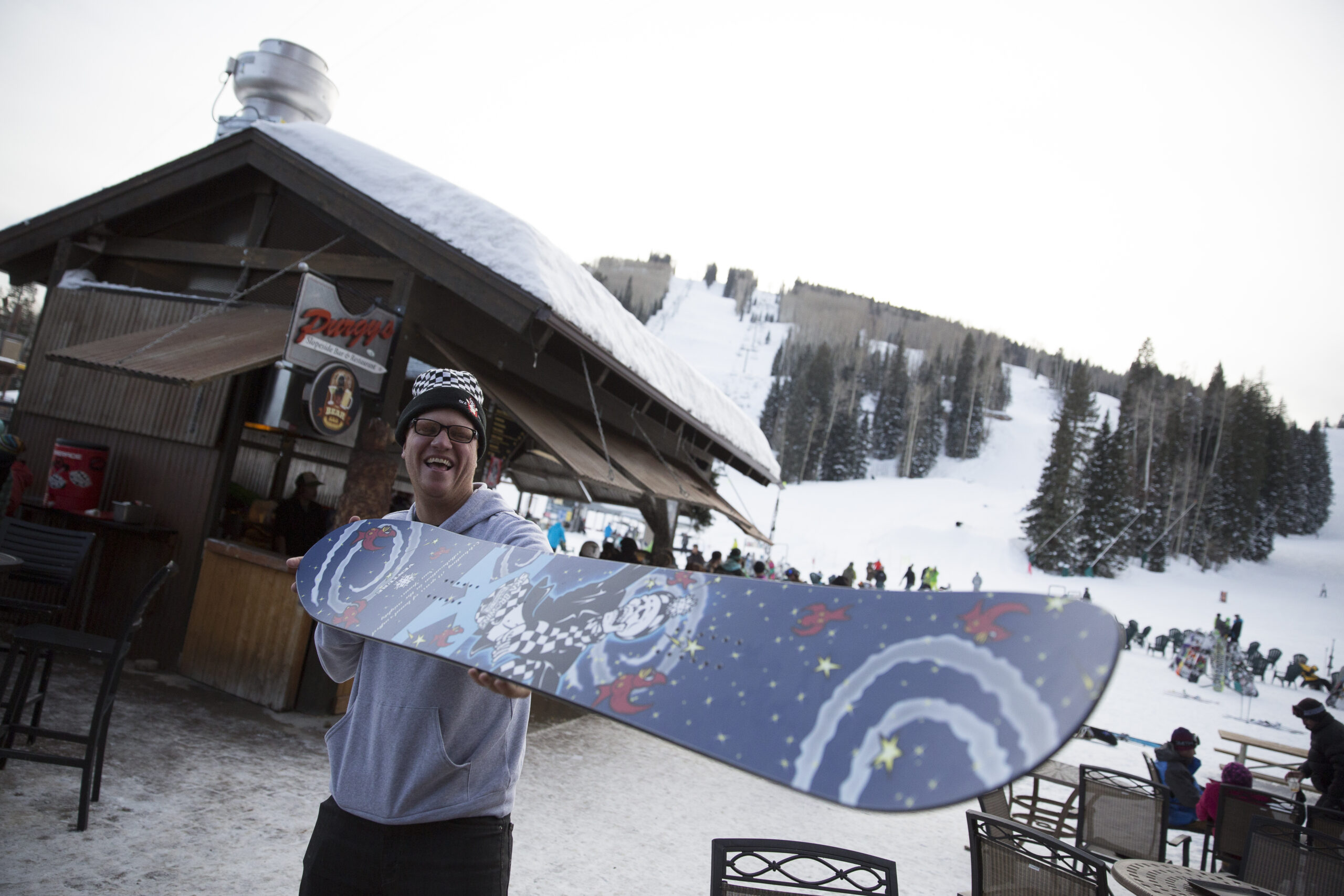 A man smiles and poses with his brand new Ska Brewing themed Venture snowboard