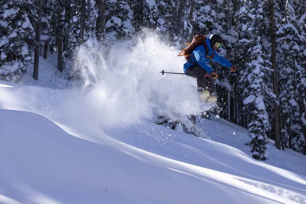 a man in blue ski gear jumps through a cloud of powdery snow