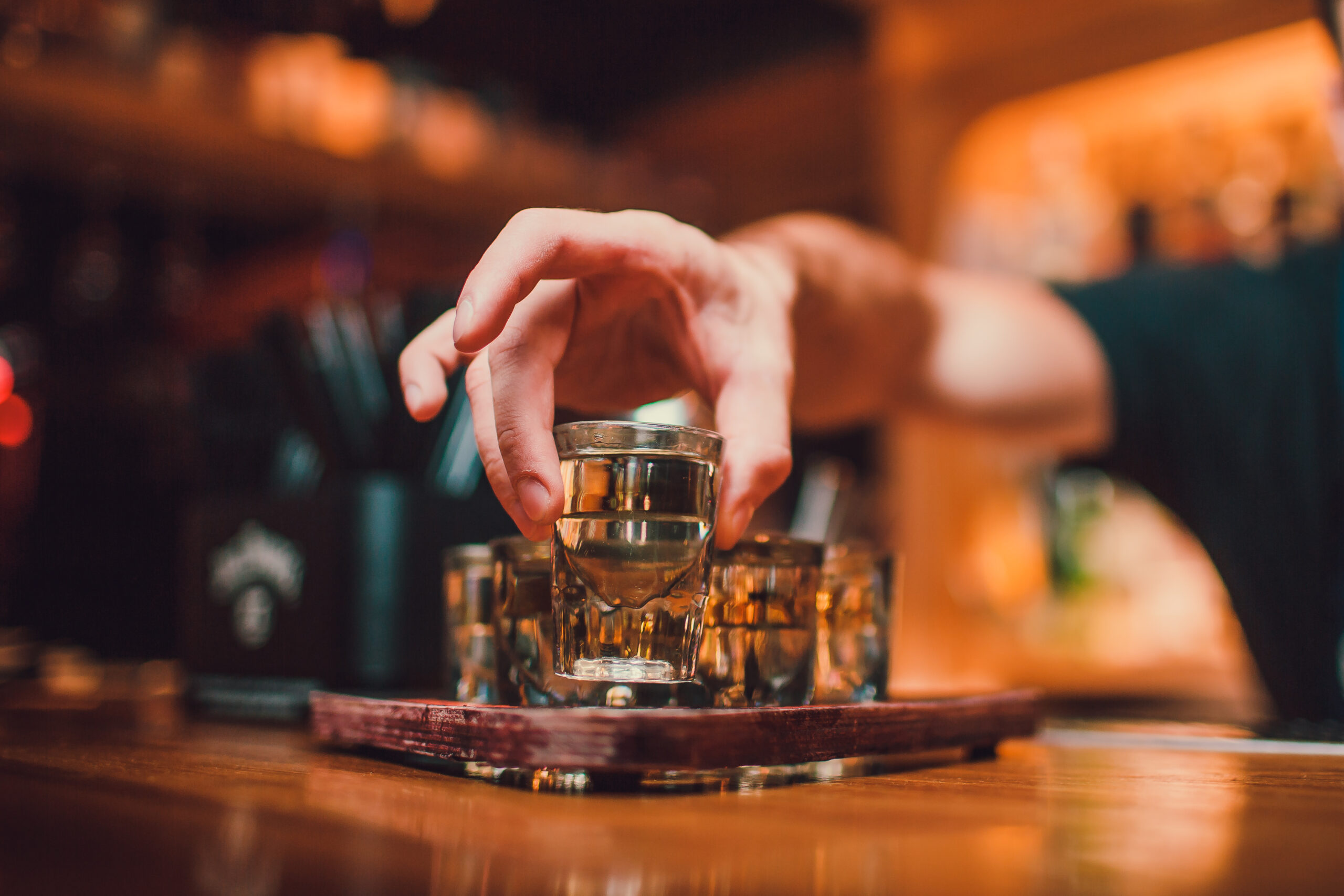 Bartender is pouring tequila into glass against the background of the bar.