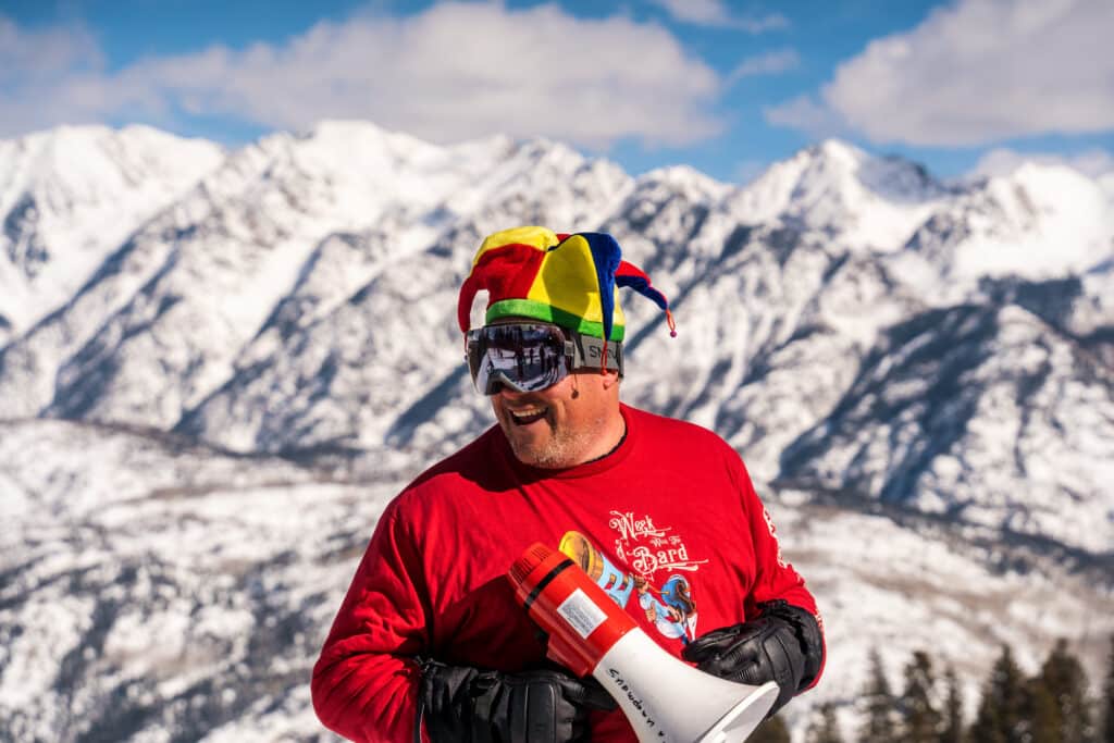 a man in a jester hat holds a megaphone in front of a mountain scene