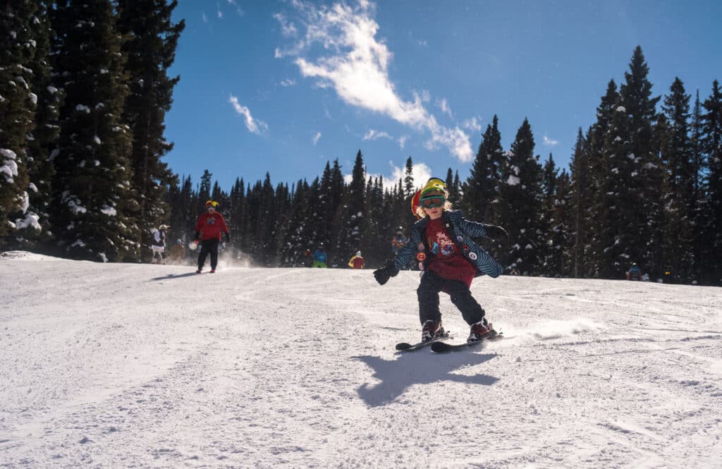 A kid in a jester hat skis down a slope