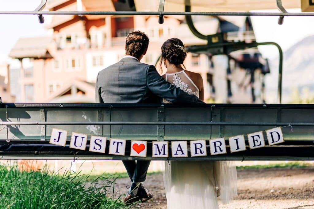 A bride and groom ride a chairlift down with "Just Married" on the back of the seat