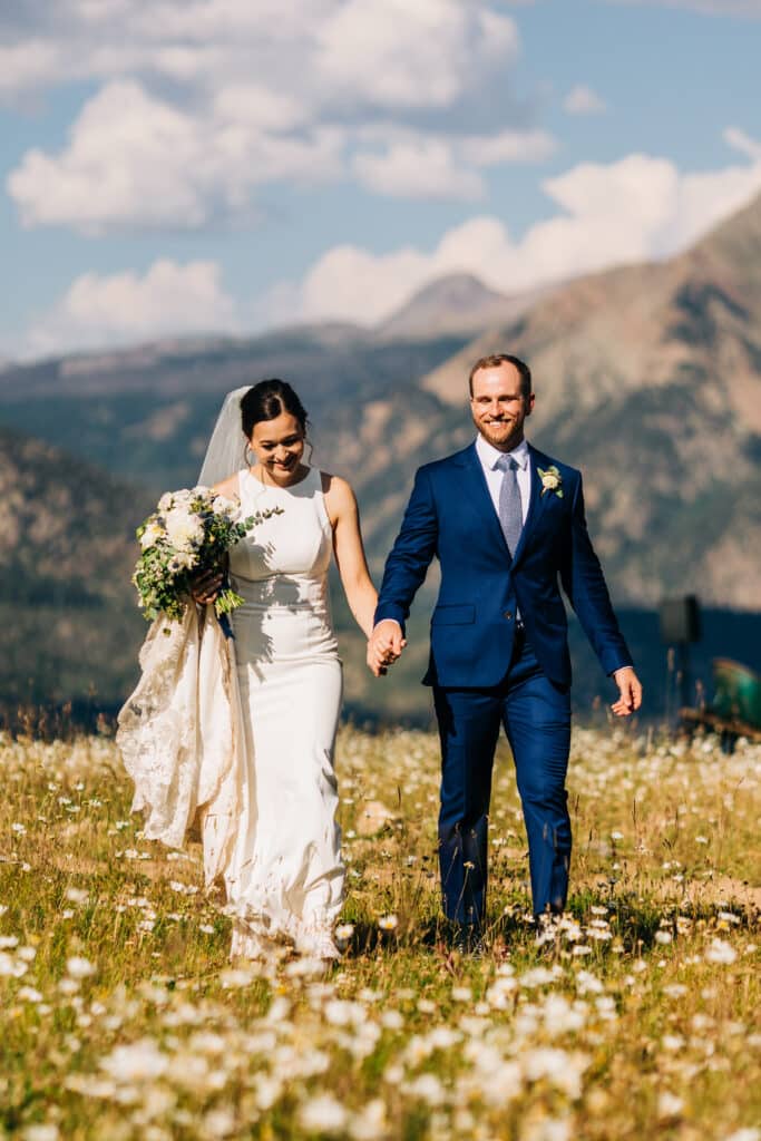 a bride and groom hold hands in a meadow