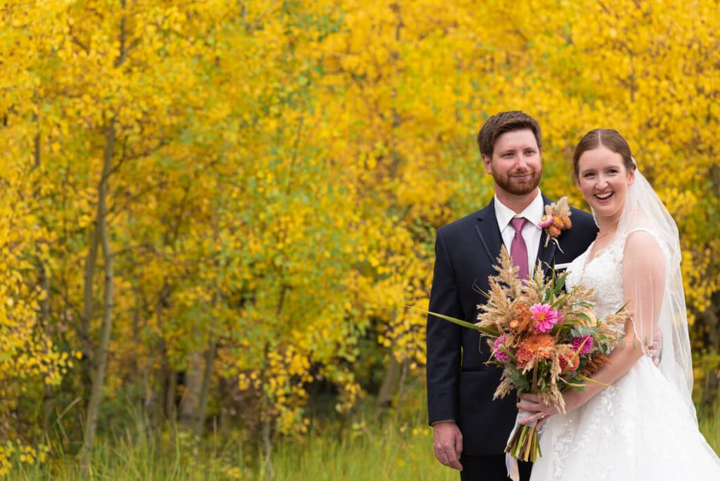a bride and groom pose with golden aspens in the background