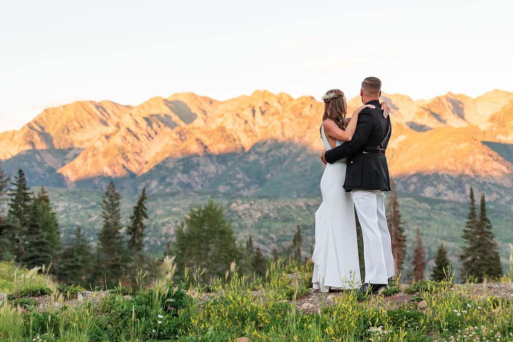 a bride and groom embrace before sun lighted mountains