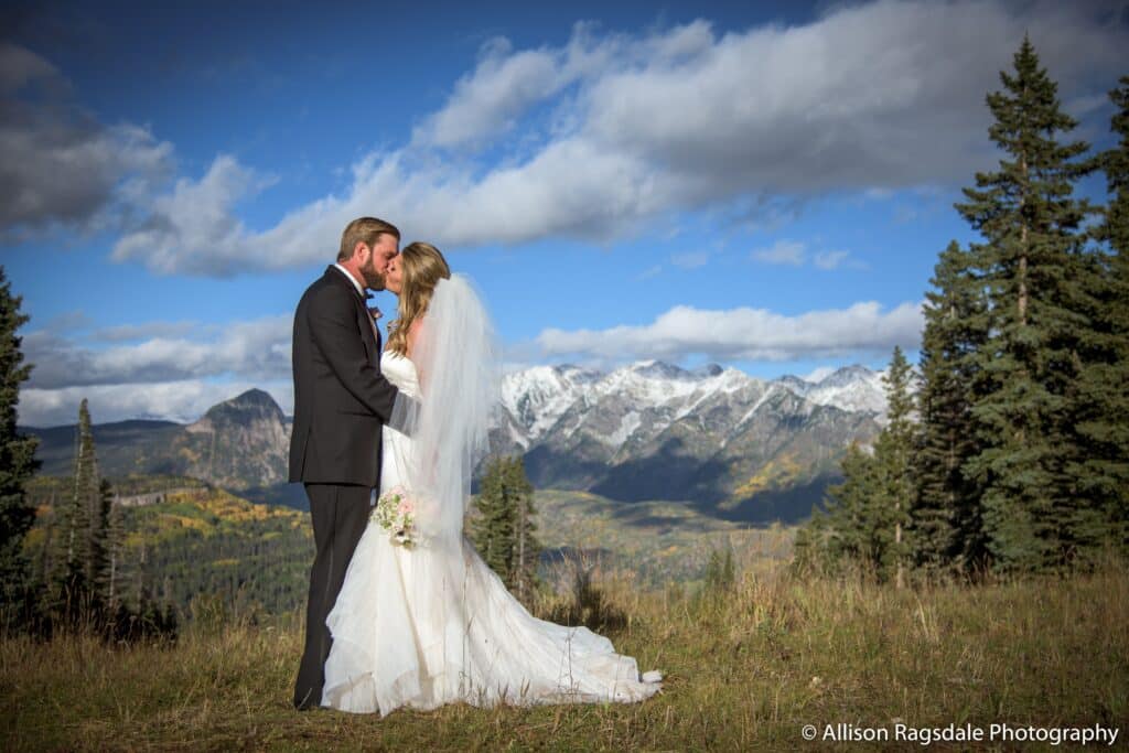 A bride and groom kissing with snowcapped mountains in the background