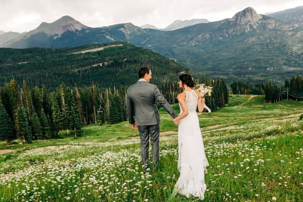 a bride and groom hold hands in a high alpine meadow