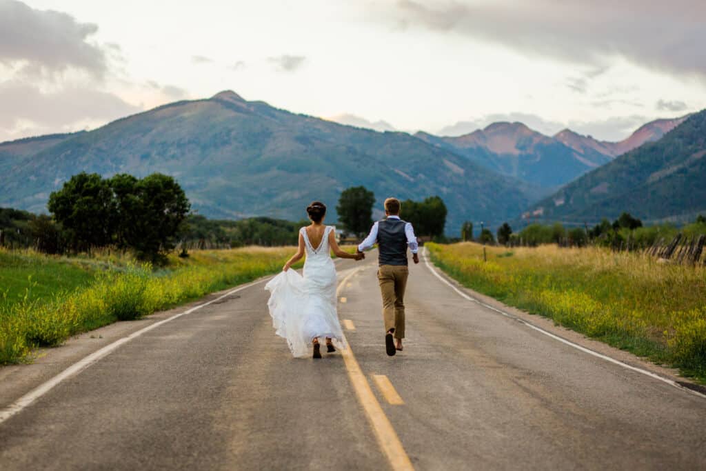 A couple walks away down an empty highway with mountains in the background