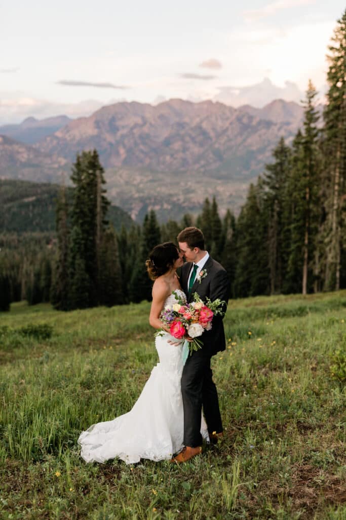 a bride and groom kiss with mountains in the background