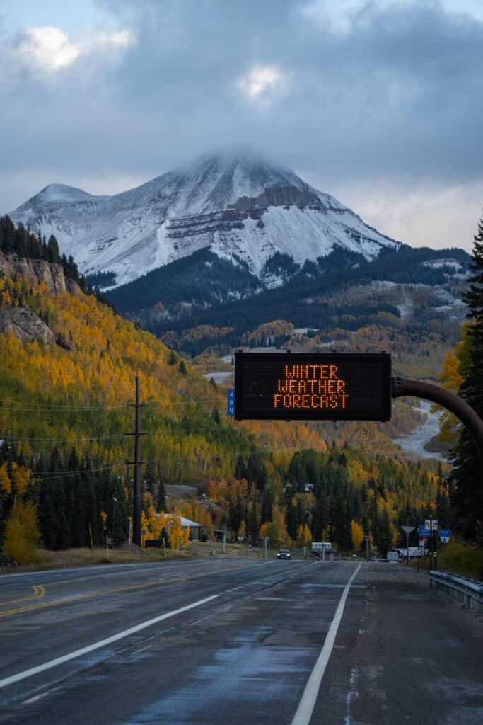 10.12.23 Fresh snow on the peaks behind a winter weather forecast sign on the highway