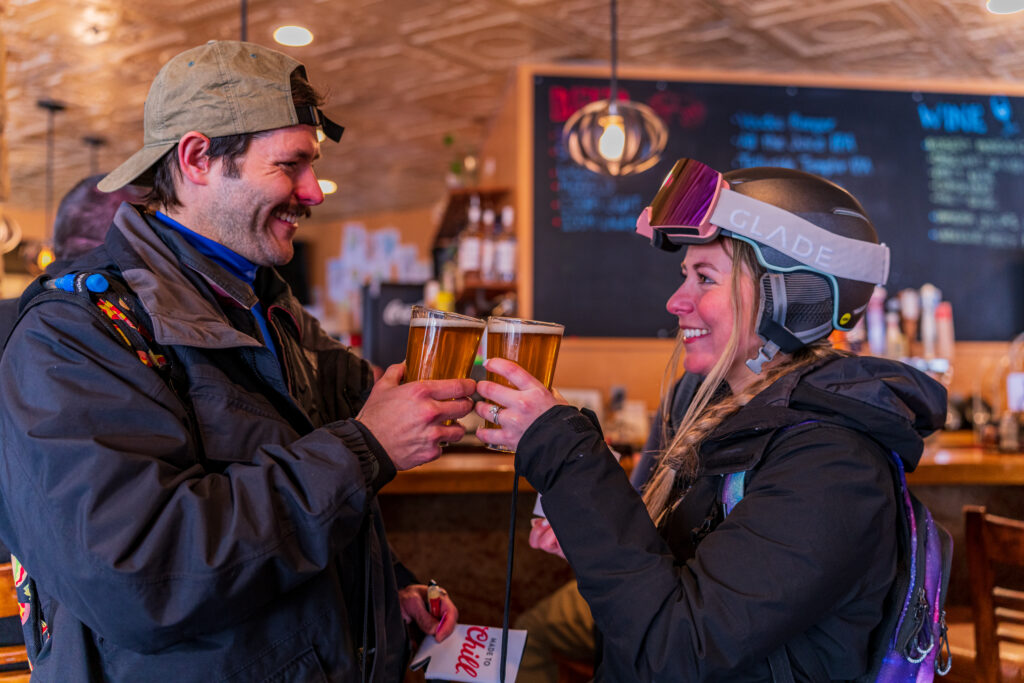 A man and woman in ski gear cheers at a bar