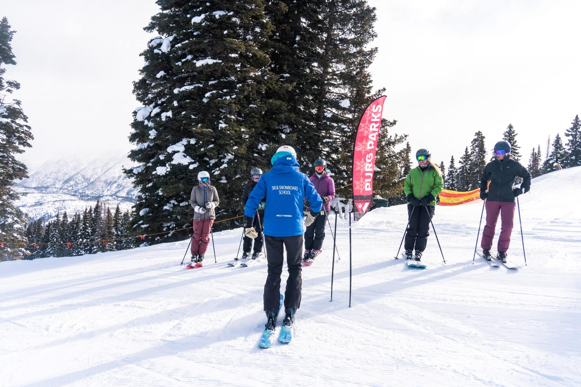 Adult ski clinic listens to instructions next to terrain park
